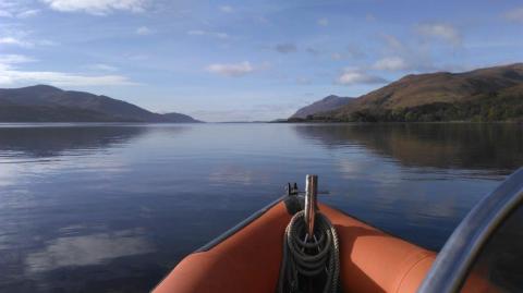 Picture shows front of orange rib, calm water and mountain ranges